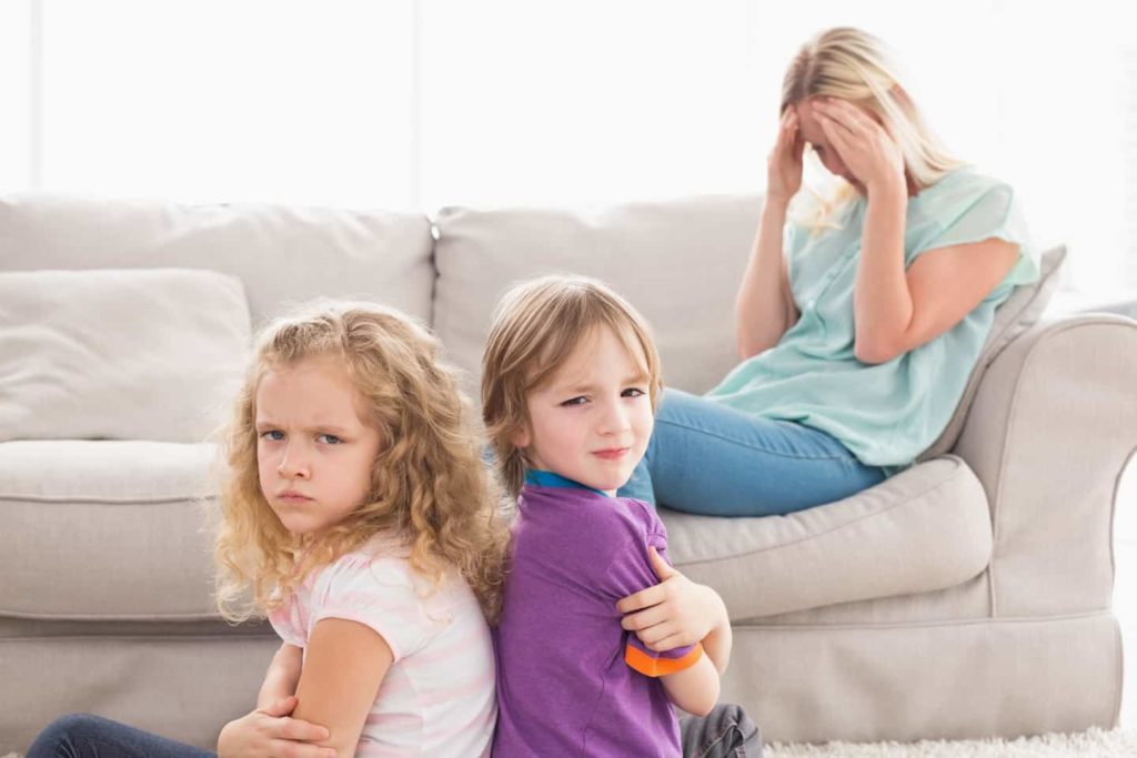 A frustrated mother sitting on a couch with her children in front of her