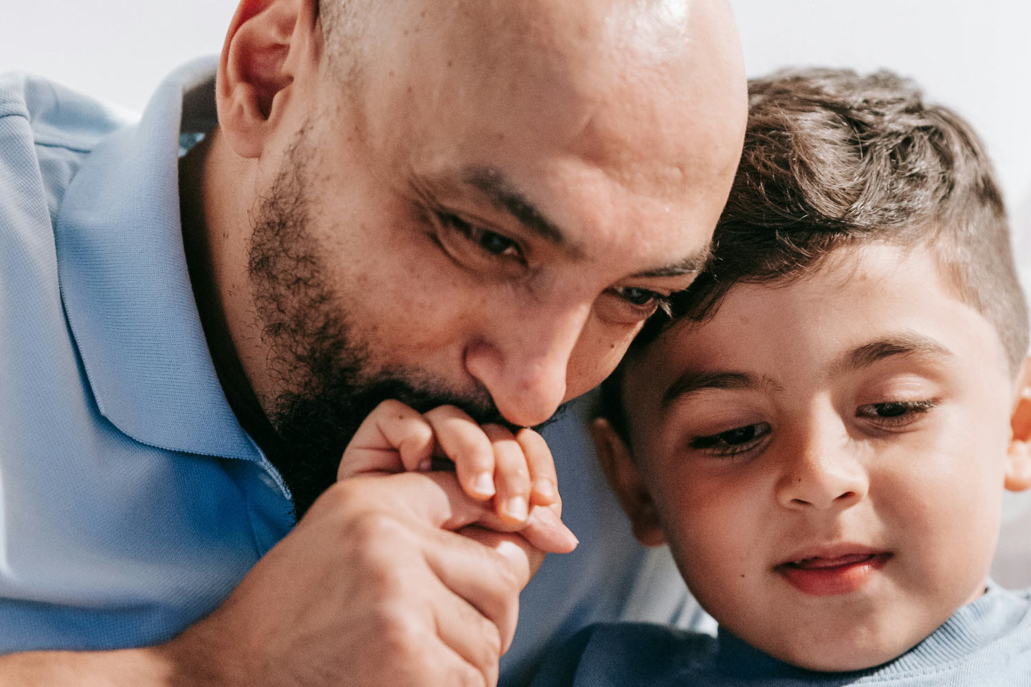 Supporting ADHD and Anxiety. A father and son sit in bed reading a book while the father kisses the boy's hand.