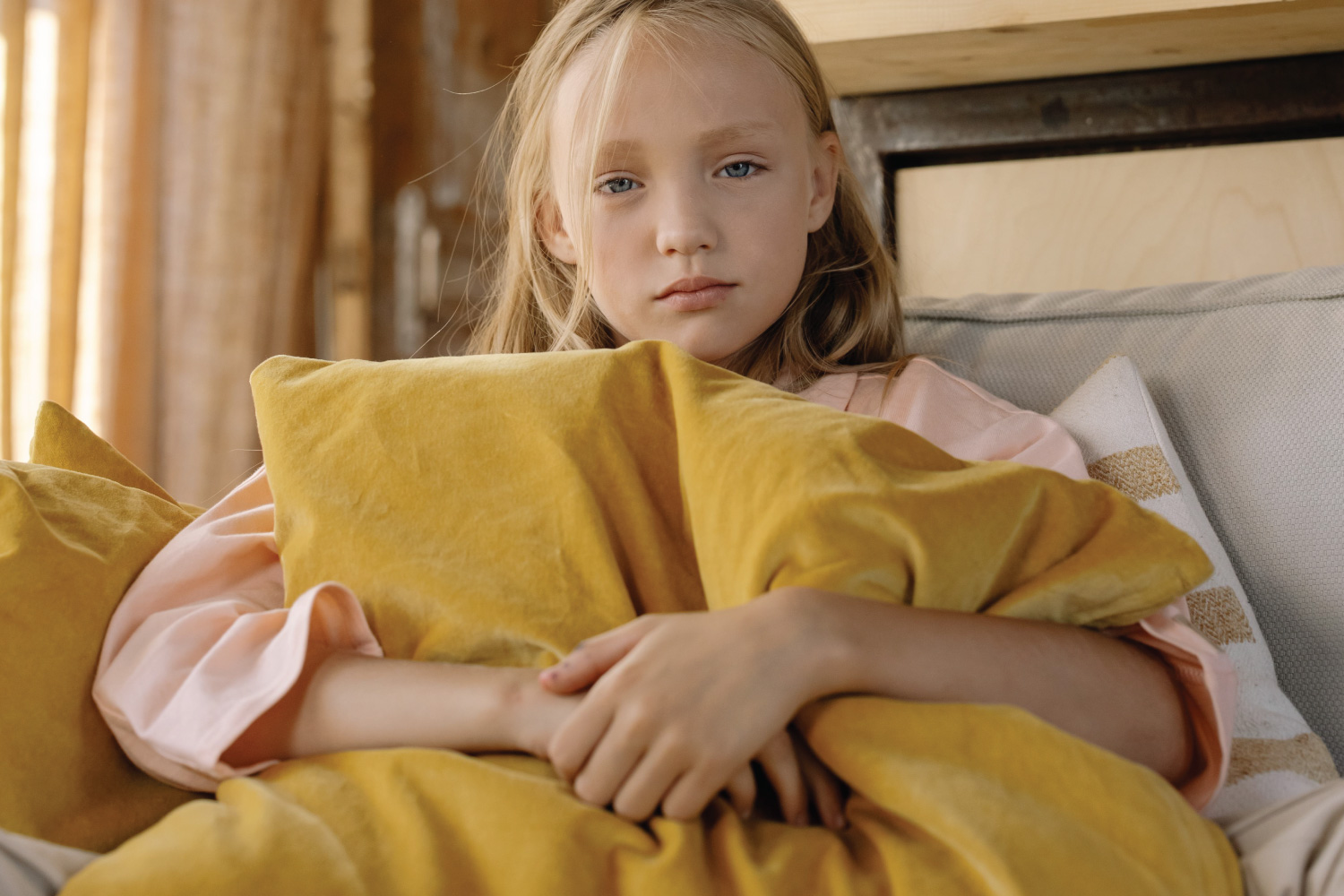 A child sits on a couch holding a pillow over their stomach with a stressed look of anxiety on their face