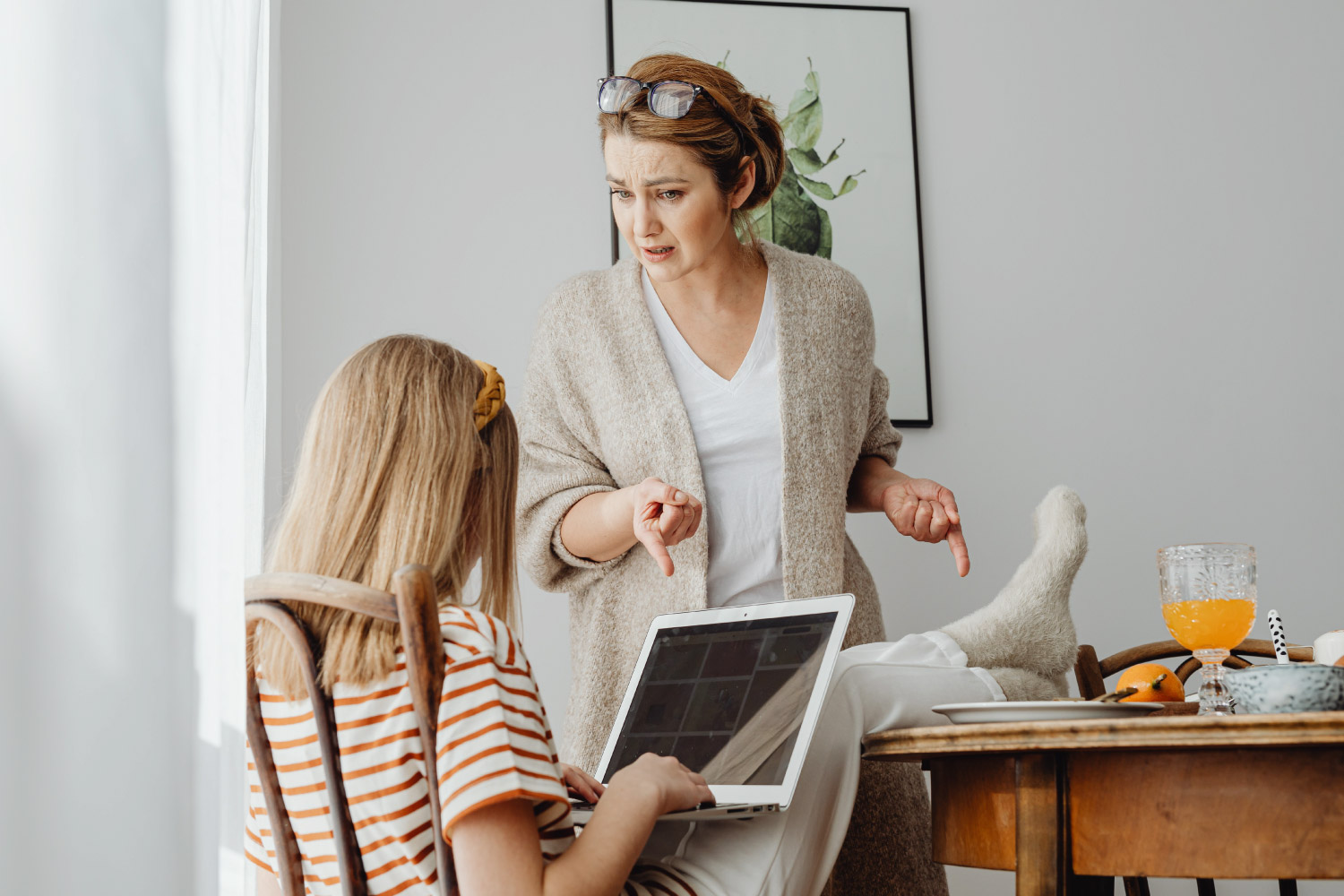 Parent talking to a young teen at the kitchen table whose on her iPad.